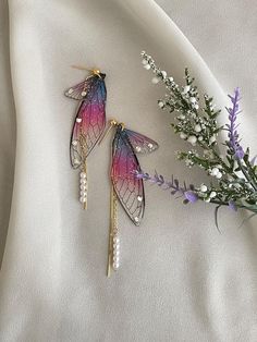 two earrings are laying on a white cloth next to some flowers and lavender sprigs