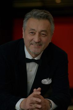 a man in a tuxedo is smiling at the camera with his hands folded