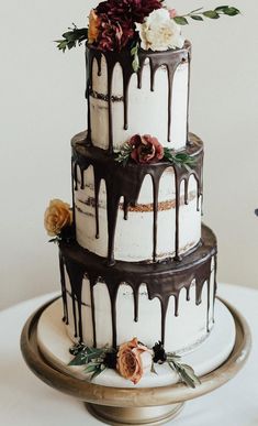 a three tiered cake with chocolate drips and flowers