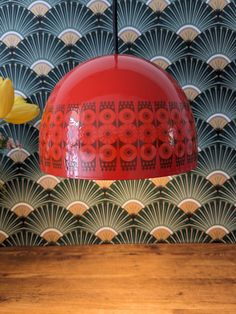 a red light hanging over a wooden table with flowers in front of a wallpapered background