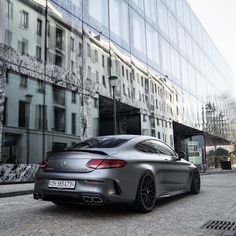 a grey mercedes cla parked in front of a large building with windows on it