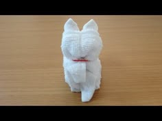 a white cat made out of toilet paper sitting on top of a wooden table with a red ribbon around it's neck