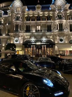 two black sports cars parked in front of a large white building with lights on it