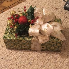 a christmas present wrapped in green and gold paper with a bow on the top sitting on a carpeted floor