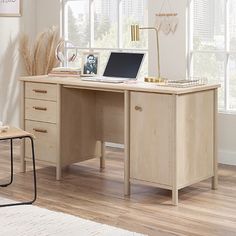 a wooden desk with a laptop on it in front of a window and a white rug