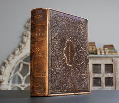 an old book sitting on top of a wooden table next to a white vase and bookshelf