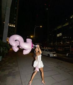 a woman in white dress holding up a pink balloon