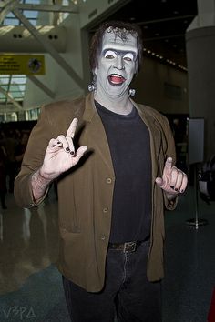 a man dressed in costume poses for the camera at an indoor event with his fingers up