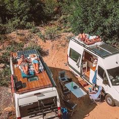 two people laying in the back of a van on top of a dirt road next to trees