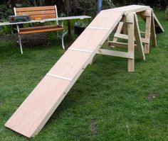 a wooden slide sitting on top of a lush green field next to a park bench