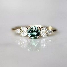 an engagement ring with a green diamond surrounded by three white diamonds on a plain surface