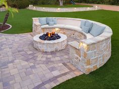 an outdoor fire pit with seating around it and lights on the side, surrounded by grass