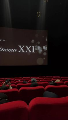 people sitting on red chairs in front of a screen with the words cinema xxii