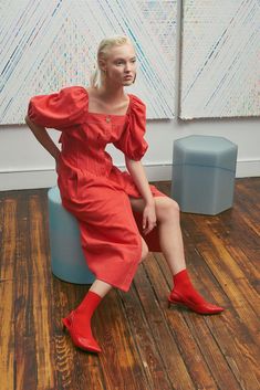 a woman in an orange dress is sitting on a blue stool and posing for the camera