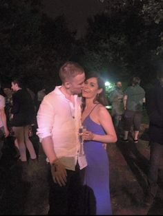 a man and woman standing next to each other in front of some trees at night