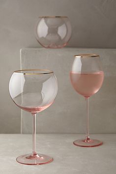 two wine glasses sitting next to each other on top of a white countertop, one filled with pink liquid and the other empty