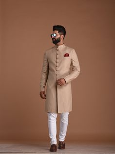 a man in a beige sherwa with white pants and brown shoes standing on a floor