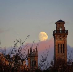 the moon is setting over some buildings and trees