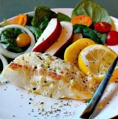 a white plate topped with fish next to a salad and lemon wedges on top of it