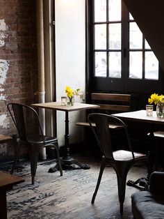 two chairs and a table with flowers in vases on them next to a window