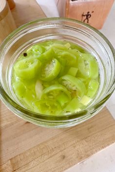 a glass bowl filled with pickles on top of a wooden cutting board