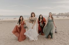 four bridesmaids walking on the beach with their bouquets