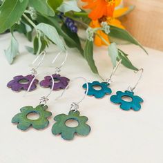 three pairs of flower shaped earrings sitting on top of a table next to some flowers