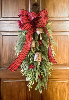 a christmas wreath hanging on the front door with bells and evergreen leaves attached to it