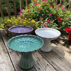 three vases sitting on top of a wooden deck next to plants and flowers in the background