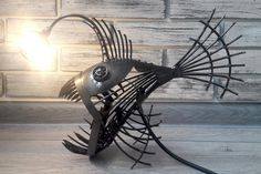 a metal fish lamp sitting on top of a wooden floor next to a brick wall