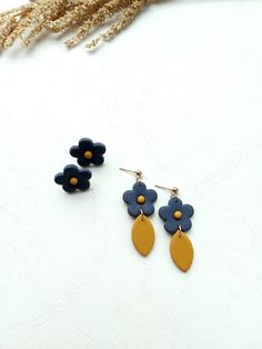 two pairs of blue and yellow flower earrings on top of a white surface with dried grass