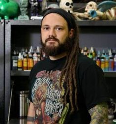 a man with dreadlocks standing in front of a shelf full of bottles and cans