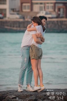 two people hugging each other by the water