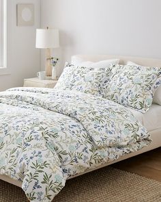 a bed with white sheets and blue flowers on it in a room next to a window