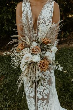 a woman in a wedding dress holding a bouquet with flowers and feathers on her back