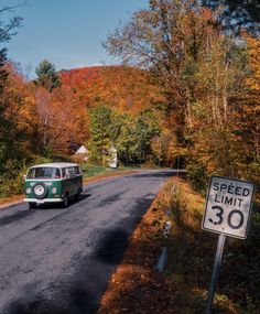 an old vw bus driving down the road in front of a speed limit sign