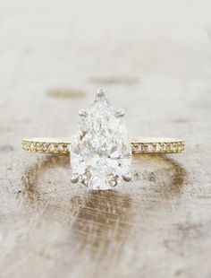 a pear shaped diamond engagement ring sitting on top of a wooden table