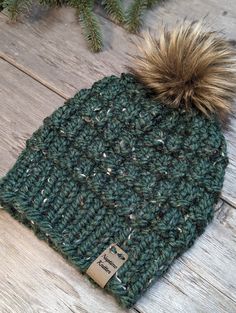 a green knitted hat with a brown pom - pom sitting on top of a wooden floor