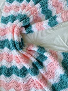 a crocheted blanket laying on top of a bed next to a white pillow