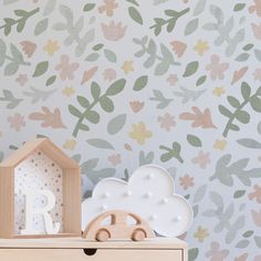 a wooden toy car sitting on top of a dresser next to a flower wallpaper