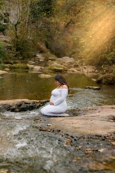 a pregnant woman sitting on rocks in the water with her hands behind her back as she meditates