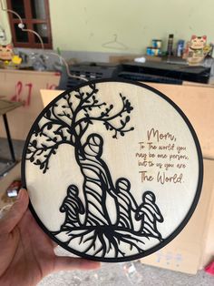 a person holding up a wooden plaque with an image of a tree and the words mom