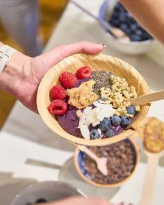 a person holding a wooden bowl filled with cereal and berries