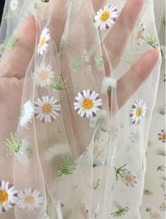 someone is holding out their hand with daisies on the sheered fabric behind them