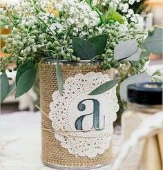 a vase filled with white flowers and greenery on top of a tablecloth covered table