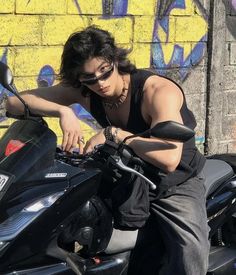 a man sitting on top of a motorcycle in front of a yellow wall with graffiti