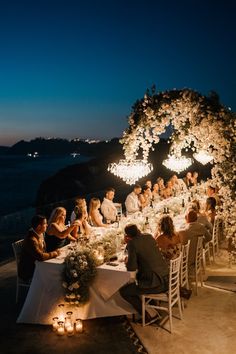 a group of people sitting around a dinner table with lit candles on the side of it