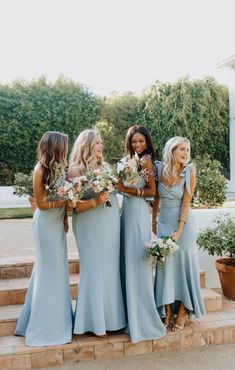 a group of women standing next to each other in blue dresses and holding bouquets