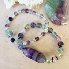 "These soothing Fluorite Beaded Bracelets are so fun! The gorgeous natural stone beads vary in colors including greens, purples and blues. The bracelets have silver plated accent beads including one with a heart. You have a choice of two stretch bracelets: #1 Medium Center Bead Bracelet - 6mm round beads with a 13-14mm pebble center bead and one Celtic heart bead. #2 Large Center Bead Bracelet - 8mm round beads with a 33mm x 14mm faceted oval center bead. Both styles are very pretty and unique. Multicolor Amethyst Natural Stones Bracelet, Multicolor Amethyst Beaded Bracelets With Natural Stones, Multicolor Amethyst Gemstone Beaded Bracelets, Multicolor Amethyst Bohemian Bracelets, Fluorite Natural Stone Beaded Bracelets As Gift, Bohemian Multicolor Amethyst Beaded Bracelets, Multicolor Amethyst Crystal Necklaces For Healing, Fluorite Bracelet, Chalcedony Bracelet