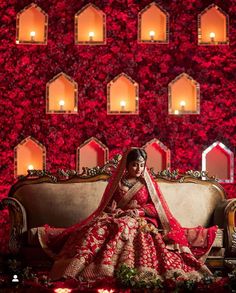 a woman sitting on top of a couch in front of a red wall with candles